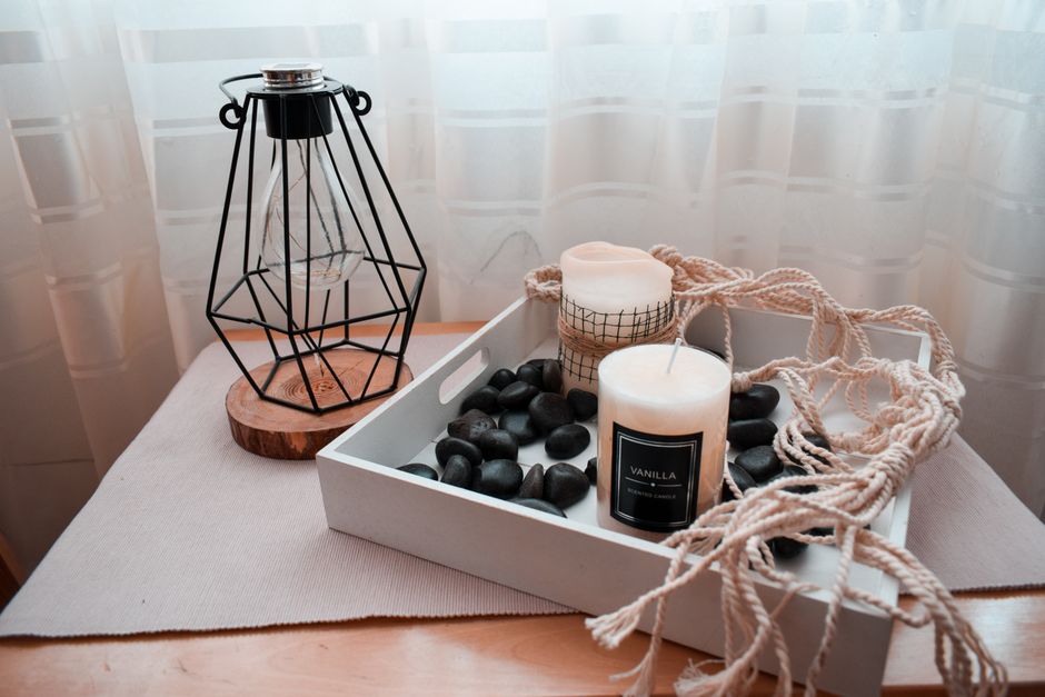 Decorative still life featuring scented candles, a lantern, and black pebbles on a wooden table.