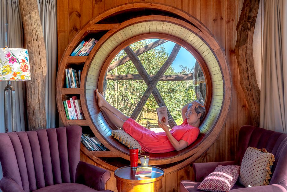Woman relaxing in a circular window reading nook, surrounded by books, enjoying a peaceful day indoors.
